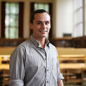 Male student with hair in bun standing in library reading room.