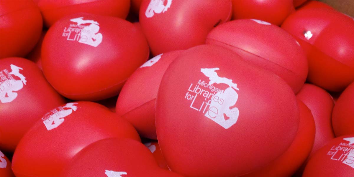 A pile of red heart-shaped stress balls imprinted with the Michigan Libraries for Life logo