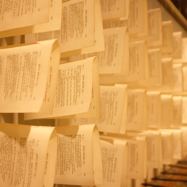 Folio pages from books, each hanging on its own support in an exhibit display