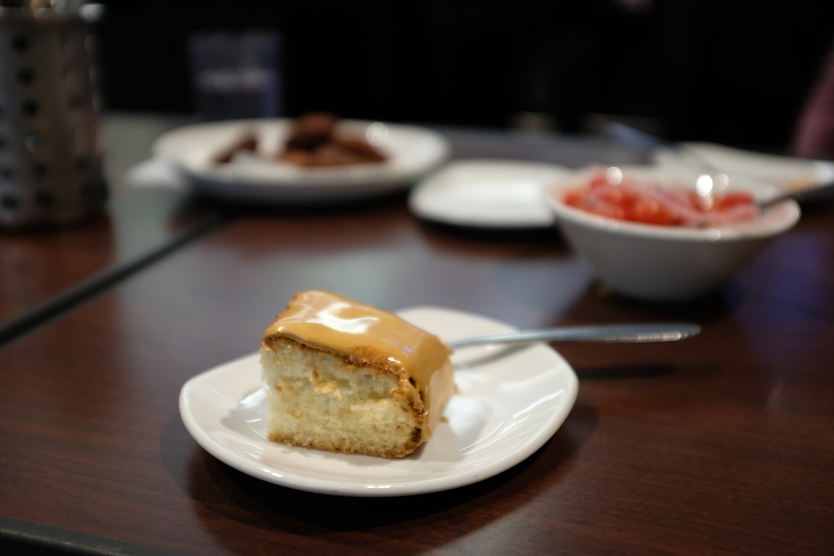 Photo of a piece of cake on a plate, and two indistinct food items in the background