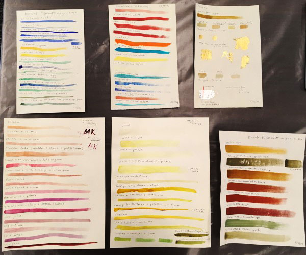 six pieces of paper, each containing painted horizontal lines in a range of color families. One of the pages contains splotches of metallic gold and silver